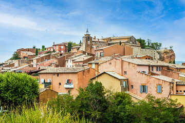 Fototapeta na wymiar Old Provencal village on a cliff with houses from ocre clay behind bushes - Rousillon, Provence, France