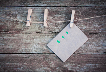 Christmas envelope with picture of green fir trees hanging on a rope with clothespins on a rustic wooden background. The concept of Christmas letters and greetings.