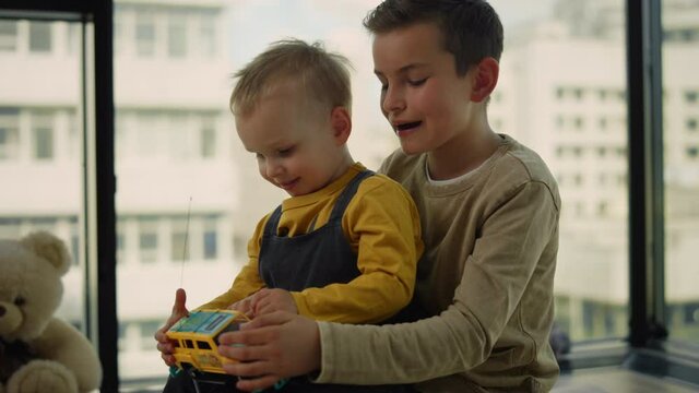 Younger brother sitting in older laps on carpet. Children playing toy car.