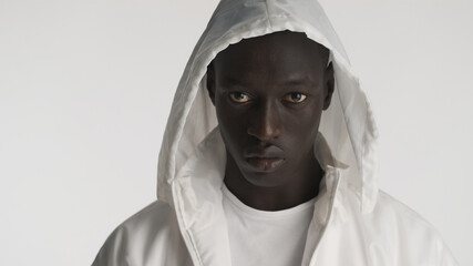 Portrait of African American man dressed in white jacket with hood posing on camera with serious look isolated on white background