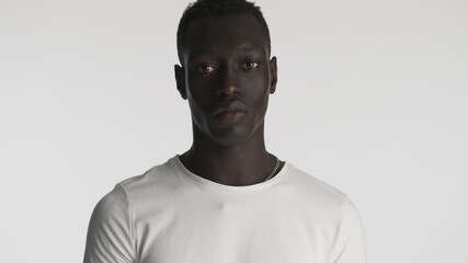 Obraz premium African American guy wearing white t-shirt posing on camera with serious look over white background