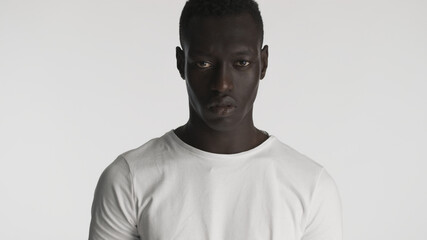 Angry African American guy wearing t-shirt  looking aggressive on camera with over white background