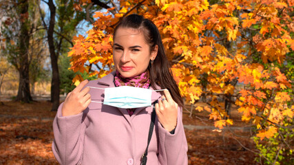 Young attractive woman put on a face mask and having fun outdoors. Covid-19 prevention by wearing protective mask on a street