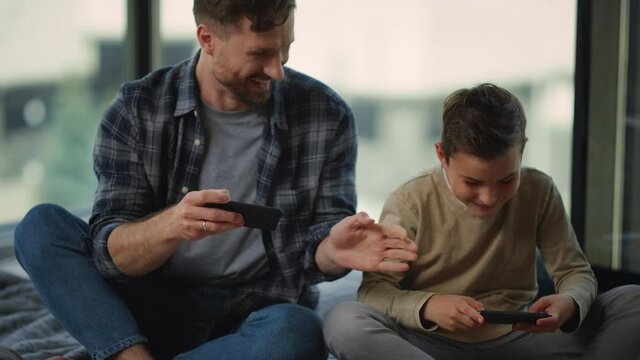 Father and son gaming mobile phones. Dad and boy spying each other smartphones.