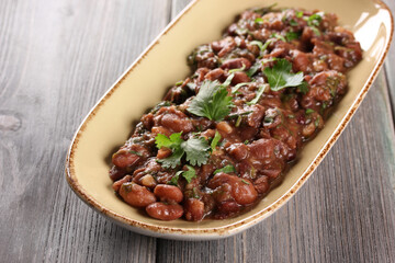 Georgian cuisine. Mingrelian lobio. Appetizer of stewed red beans, onions, garlic, spices and herbs in a beige plate on a wooden background. Background image, copy space. Restaurant menu. Horizontal