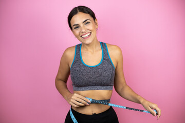 Young beautiful woman wearing sportswear over isolated pink background smiling with a measuring tape around her waist