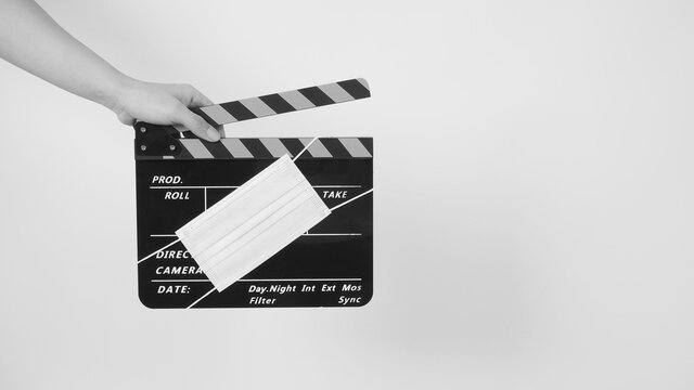 Hand is hold clapper board or movie slate with face mask. it use in video production and cinema industry on white background.In black and white picture.