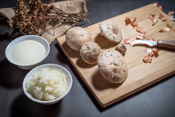 Top view of fresh white mushrooms on a wooden cutting board with chopped onions and sauce in bowls