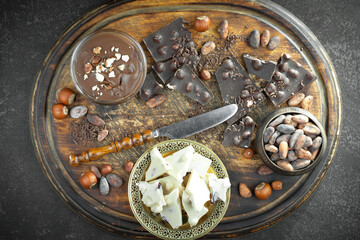 White and black chocolate on the table in a composition with nuts and cocoa beans.