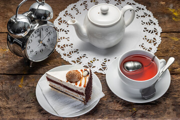 Five o'clock tea. White tea set on an old wooden table with cake, alarm clock and tea strainer. In the style of Alice in Wonderland