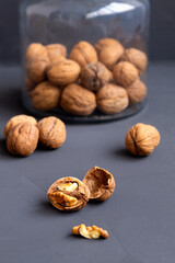 close-up peeled walnuts in shells on a black table and in a glass jar. brown nuts on a dark background. copy space. vertical. dried walnut and fruit. 