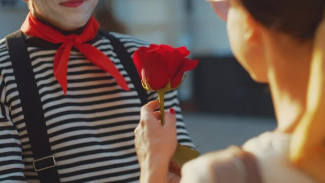 Young mime giving a rose to a girl, close-up