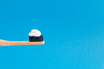 Closeup on bamboo toothbrush with white paste on the blue background