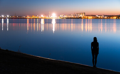 Silhoette of woman looking at night lights of town reflected in sea 