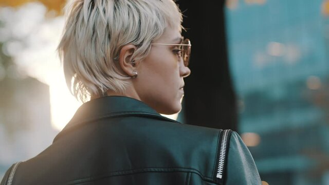 Beautiful short haired blond woman in leather jacket and sunglasses turning her head toward camera . High quality 4k footage