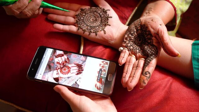 Woman getting a henna tattoo mehendi design copied from phone onto her hand for the bride bridesmaid shaadi event or a hindu festival like karwachauth diwali holi and teej