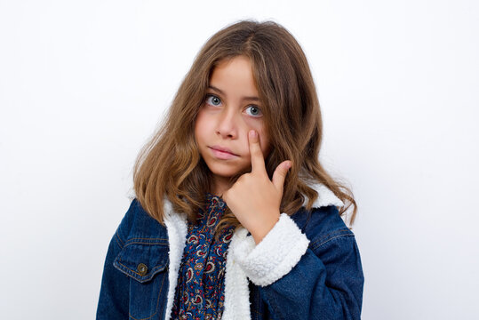 Little caucasian girl with beautiful blue eyes wearing denim jacket standing over isolated white background Pointing to the eye watching you gesture, suspicious expression.