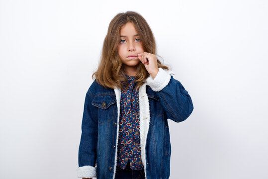 Little caucasian girl with beautiful blue eyes wearing denim jacket standing over isolated white background mouth and lips shut as zip with fingers. Secret and silent, taboo talking.