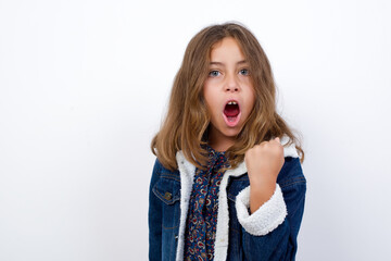 Little caucasian girl with beautiful blue eyes wearing denim jacket standing over isolated angry and mad raising fist frustrated and furious while shouting with anger. Rage and aggressive concept.