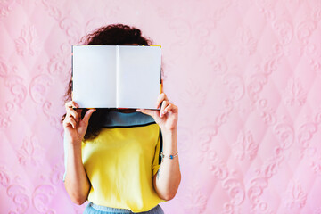 The girl is holding a book with white pages for copy paste on a yellow background and eating Lollipop . You can add your own text or image.