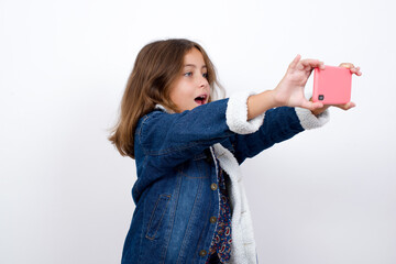 Little caucasian girl with beautiful blue eyes wearing denim jacket standing over isolated white...