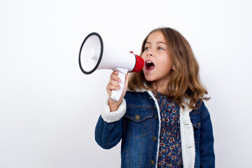 Naklejka premium Little caucasian girl with beautiful blue eyes wearing denim jacket standing over isolated white background Through Megaphone with Available Copy Space