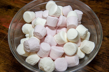 A bowl of delicious white and pink marshmallows on a brown wooden table