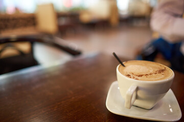 White cup of coffee with square plate on brown table in cafe. Copy space. Selective focus