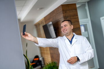 Photo of a doctor man wearing medical uniform. Smiling medic taking a selfie ready to post it on her social media.