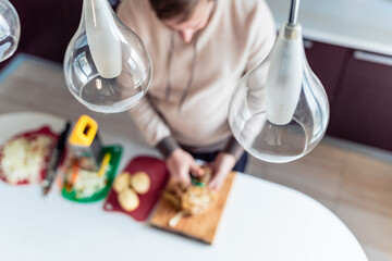 Cooking man, father, cooker. Preparation of soup, lunch, dinner in kitchen. Cutting vegetables, potatoes, carrots, onions on wooden board.Large knife.Large pot of boiling water.Surprise,help for wife