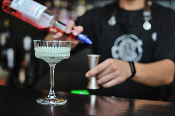 Bartender adds drink and ingredients to cocktail glass on bar counter with bar equipment