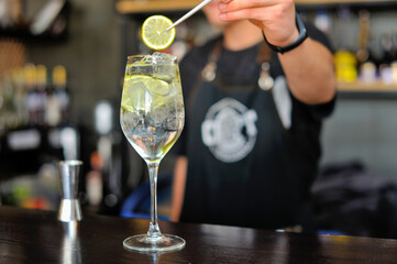 Bartender adds drink and ingredients to cocktail glass on bar counter with bar equipment