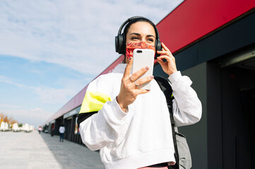 Sportsman with mask listening to music with headphones and smart phone