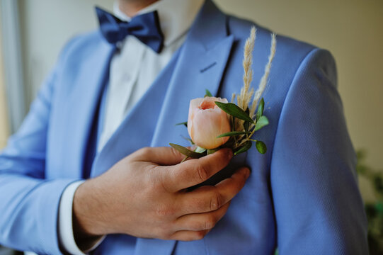 Groom wearing a suit with boutonniere pinned on the lapel in anticipation of his marriage celebration to his wife that he is in love with. Masculine combined with a feminine floral touch.