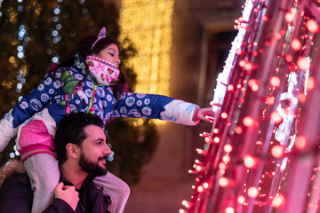 Father with little sister looking city christmas lights. Focus is on father, ambient light image.