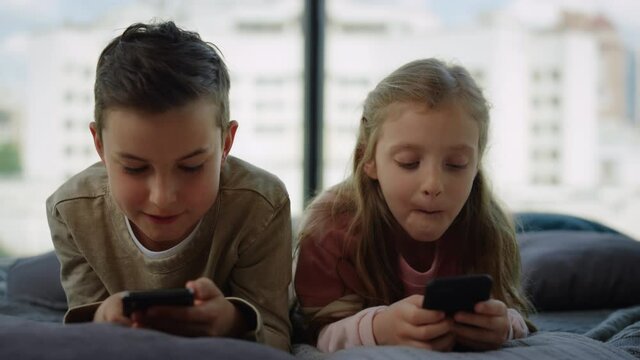 Brother and sister gaming on mobile phones. Siblings using smartphones at home.