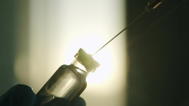 The needle of the syringe takes medicine from glass vial against the background of the setting sun. a vaccine against coronavirus sputnik v