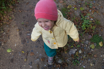 A two-year-old girl runs laughing along the road. Shooting from the upper angle.