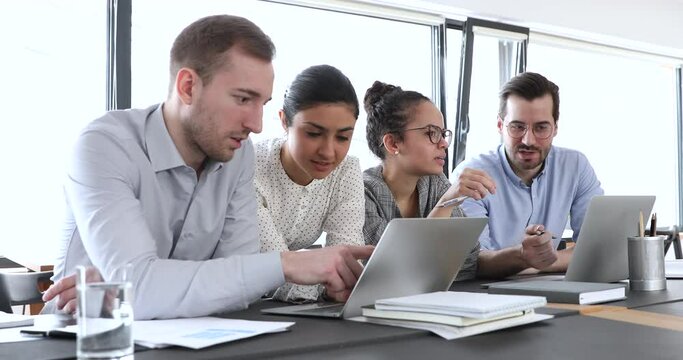 Focused young caucasian employee sharing good project results in computer application with smiling indian colleague. Busy diverse multiethnic business people involved in working processes at office.