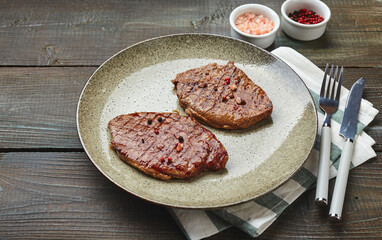 Two grilled ribeye steaks, spices and tomato-cucumber salad with sour cream on a wooden table.