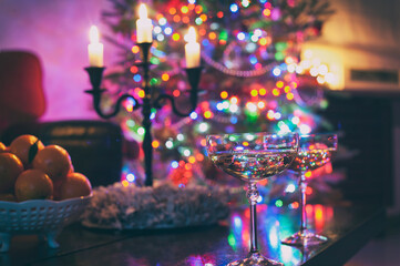 Two champagne glasses on illuminated christmas tree defocused background