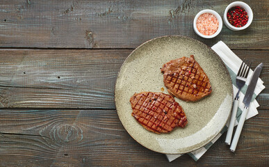 Two grilled ribeye steaks, spices and tomato-cucumber salad with sour cream on a wooden table.