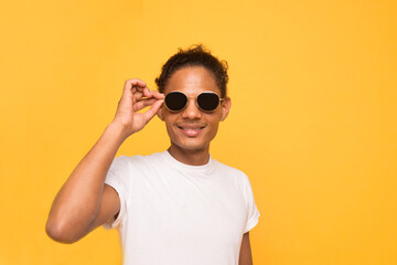 Cheerful attractive handsome guy in a white t-shirt taking off black glasses isolated on bright bright yellow background