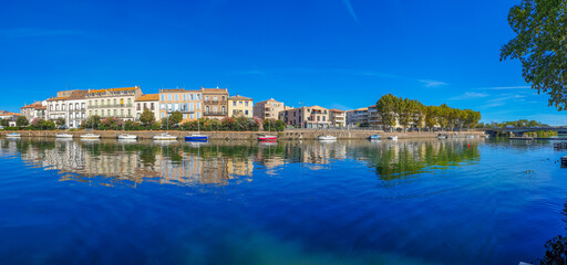Obraz premium Panorama view of Herault river at the town Agde with buildings and boats, Languedoc-Roussillon France