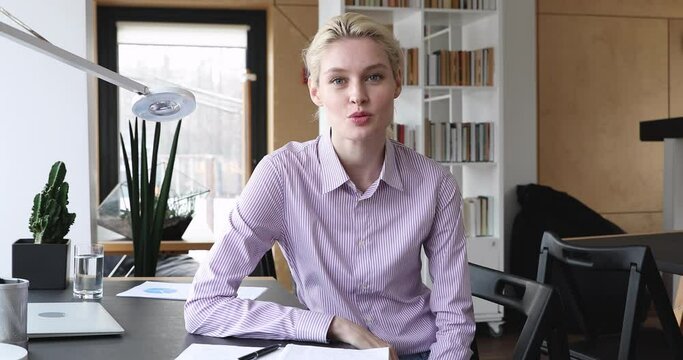 Web camera view young pretty smiling blonde woman sitting at workplace, communicating with colleagues online. Happy millennial lady talking speaking enjoying conversation, looking at camera.