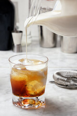 White Russian cocktail preparation. Pouring cream into the glass