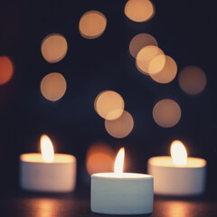 Three burning candles in front of a beautiful colorful circle shiny bokeh background