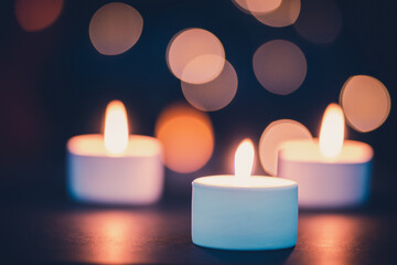 Three burning candles in front of a beautiful colorful circle shiny bokeh background