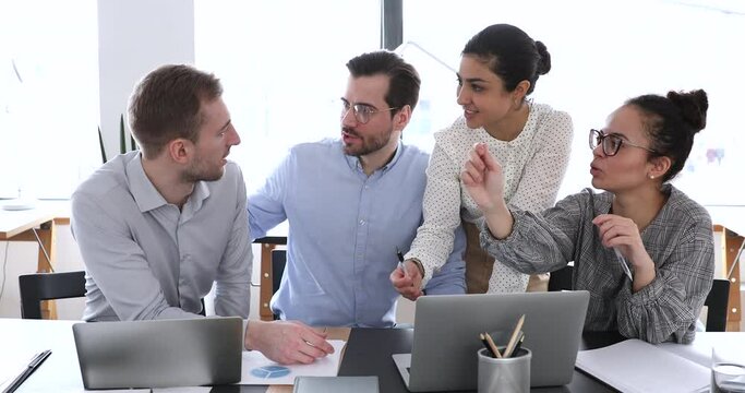 Young male employee sharing creative idea with happy diverse colleagues at briefing meeting. Group of smiling multiracial business people developing marketing strategy of startup project in office.