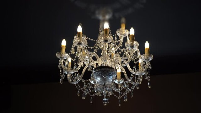 Huge crystal chandelier hanging on house ceiling in dark room, beautiful vintage chandelier with diamonds details and LED lights in candelabra. Luminous crystal lamp on ceiling
